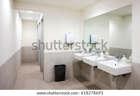 Empty public bathroom with white sinks and wide wall mirror, air hand drier and black recycle bin