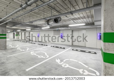 Empty public underground parking lot or garage interior with concrete stripe painted columns and signs. Electric car charging place.