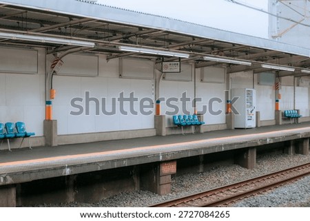 An empty railway station platform featuring blue plastic benches and a vending machine on a cloudy day in Japan