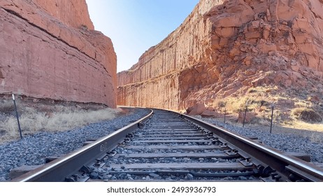 An empty railway track cuts through a red rock canyon near Moab, Utah, USA. The shot gives a sense of adventure, travel, and the vastness of nature. Taken on the Corona Arch trail. - Powered by Shutterstock