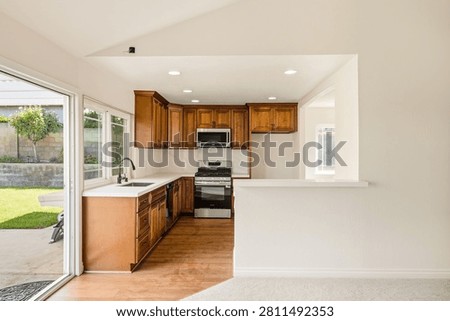 An empty, recently renovated suburban kitchen featuring rich brown wood cabinetry, stainless steel appliances, white quartz countertops, and a bright