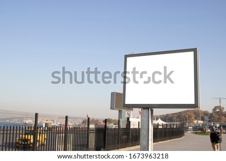 Empty rectangular bilboard. Photographed on the edge. Walking people.