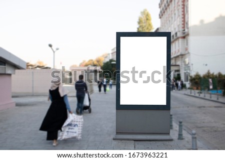 Empty rectangular bilboard. Photographed on the edge. Walking people.