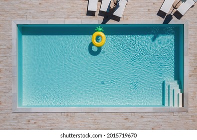 Empty rectangular blue swimming pool with sunbeds and umbrellas and big inflatable Yellow Pineapple floating tube. Rent a real estate or Chill out summer vacation in luxury resorts concept.