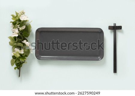 Empty rectangular gray plate for asian food with black chopsticks on blue background surface with spring branches. Asian style. View from above. Copy space. Japanese food concept.
