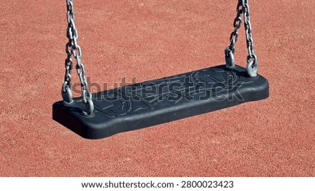 An empty rectangular rubber swing seat featuring molded decorative patterns is suspended by heavy-duty steel links above a rubberized playground floor