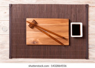Empty rectangular wooden plate for sushi with sauce and chopsticks on wooden table, top view.