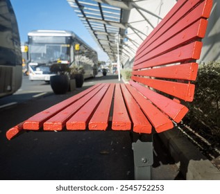 Empty red bench at the bus stop. Out-of-focus buses along the road. Auckland. 