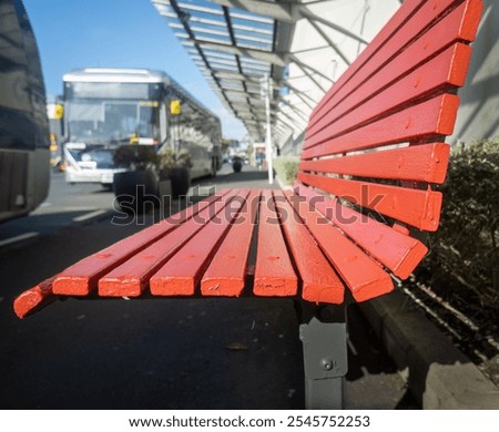 Empty red bench at the bus stop. Out-of-focus buses along the road. Auckland. 