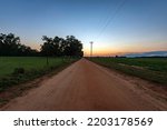 Empty red dirt road leading into the sunset with pasture on one side and peanut field on the other.