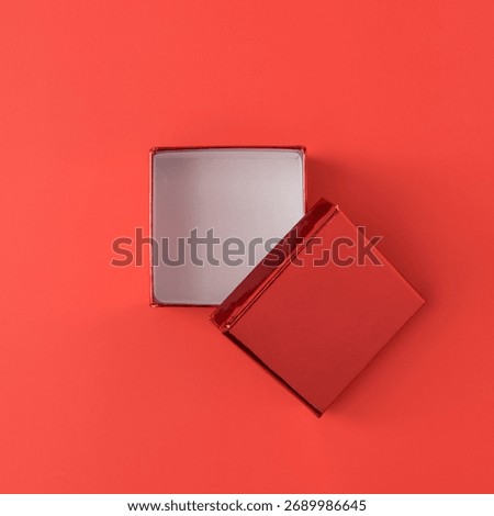 Empty red gift box with lid on coral red background. Clean minimal Christmas still life capturing quiet anticipation. Minimal festive still life with elegant tones.