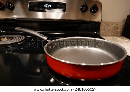 An empty red and grey frying pan Skillet sits on the stove top.