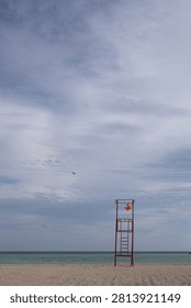 Empty red lifeguard tower frame with a tattered warning flag on a deserted pebble beach, seagulls flying over the calm sea.