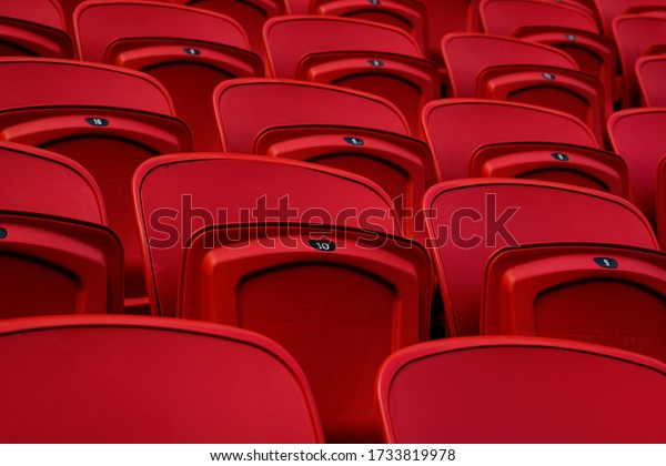 Empty red plastic seats in an empty stadium. Many\
empty seats for spectators in the stands. Empty plastic chairs\
seats for football fans.