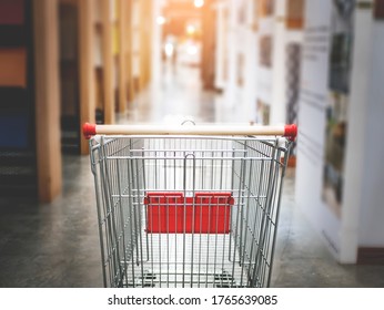 Empty Red Shopping Cart Trolley In Super Market Store Aisle Representing Stocking Products, Buying Food Hording Supplies For Storing Food In Home Or Small Retail Shop, Purchasing Goods And Produce 