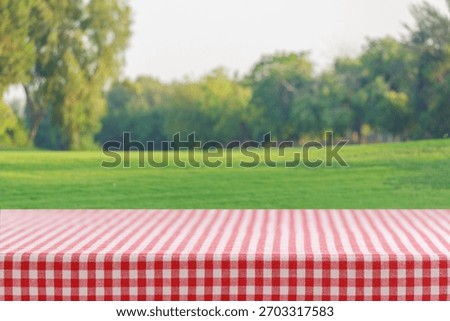 Empty red and white checkered tablecloth for picnic over background of lawn with fresh green grass and trees 