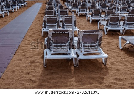 Empty resort beach with rows of sunbeds on sand beside wooden boardwalk path.