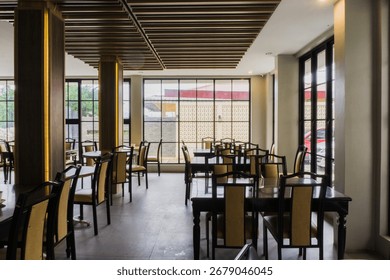 Empty restaurant interior with many dark wood tables and chairs, large windows, and a wood slat ceiling.