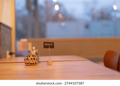 Empty restaurant interior table with candle and small reserved sign, warm evening bokeh, wooden tabletop, soft yellow lighting, urban window view, intimate datenight mood.
