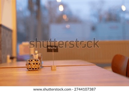 Empty restaurant interior table with candle and small reserved sign, warm evening bokeh, wooden tabletop, soft yellow lighting, urban window view, intimate datenight mood.
