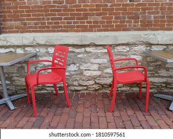 Empty Restaurant Patio Tables With Red Chairs On A Brick Sidewalk