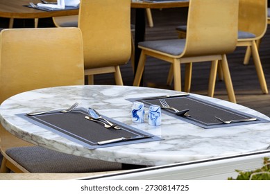 Empty restaurant table with marble surface, cutlery and table setting. Modern cafe interior, cozy atmosphere, dining concept, restaurant service and hospitality background.