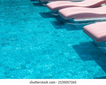 The empty retro style of pink color curved sunbeds, chairs on the blue swimming pool in a hotel resort on sunny day, summer holiday vacation background concept.