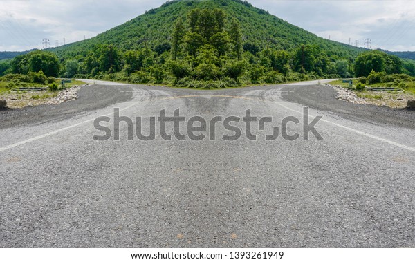 Empty road is divided into two different ways.\
Dirt or rough long road in countryside leading to distant towards\
bright sun in forest. Low view of empty roadtrip road ground /\
surface. Hope concept.