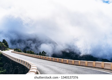 Empty road high in the mountains with cloudy foggy sky