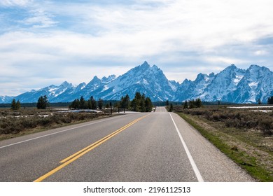 Empty Road Highway Facing The Grand Teton Mountain Range Under Dramatic Cloudy Sky Wide Angle Lens No People