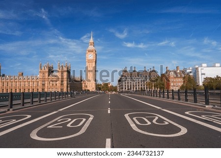 Empty road leading towards Big Ben and Westminster palace. Numbers and signs on bridge during sunny day. Famous tourist attraction with blue sky in background.