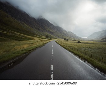 Empty road in a misty Scottish valley, surrounded by rugged mountains under cloudy sky. Moody, tranquil atmosphere, Scotland's wilderness remote countryside landscape, travel, nature and exploration. - Powered by Shutterstock