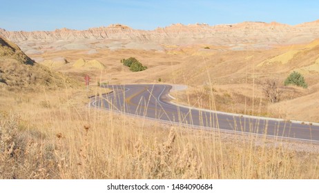 Empty road snaking through endless Badlands landscape with rocky sandstone formations. Empty road winding across the stunning Badlands desert in South Dakota. Road trip across the sunny United States.