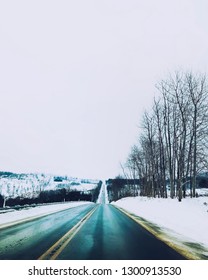 Empty road surrounded by snow and trees.