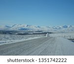 Empty road in winter with snow on the road, snow-covered mountains, and blue sky