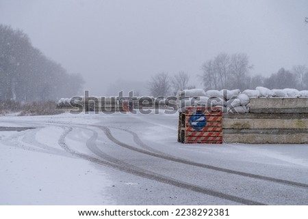 empty roadblock on the road. concrete slabs, sandbags and anti-tank hedgehogs restrict traffic. military structures on a winter road. blizzard and ice on the road at the patrol post. war in ukraine