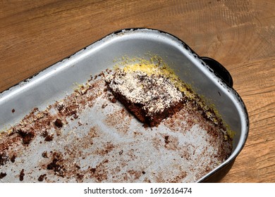 Empty Roasting Pan. The Last Piece Of Cake In An Old Enamel Empty Baking Pan. The Rest Of Brown Cocoa Buns. Roasting Pan On Wooden Table.