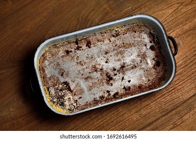 Empty Roasting Pan. The Last Piece Of Cake In An Old Enamel Empty Baking Pan. The Rest Of Brown Cocoa Buns. Roasting Pan On Wooden Table.