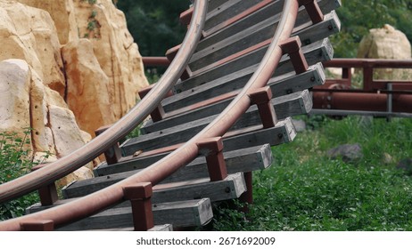 Empty roller coaster track curves through lush greenery in an amusement park on a cloudy day