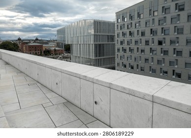 Empty rooftop terrace with light stone tiles overlooking modern office buildings under a cloudy sky in a quiet city setting.