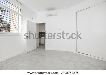 An empty room with a bay window in a loft-style house with a two-section built-in wardrobe with white wooden sliding doors