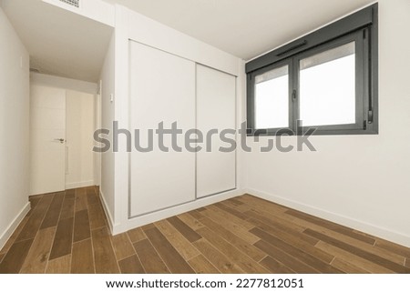 Empty room with a built-in wardrobe with white wooden sliding doors, black anodized aluminum windows and dark stoneware floors Foto d'archivio © 