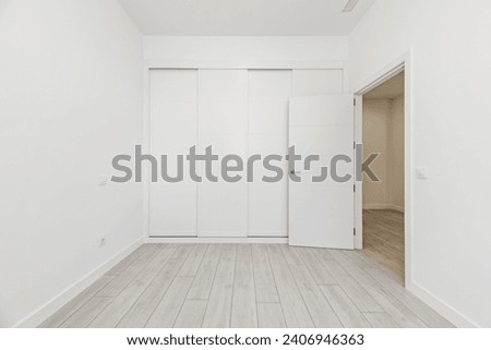 An empty room with built-in wardrobes with white sliding doors along one wall, white wooden carpentry with access door to other rooms