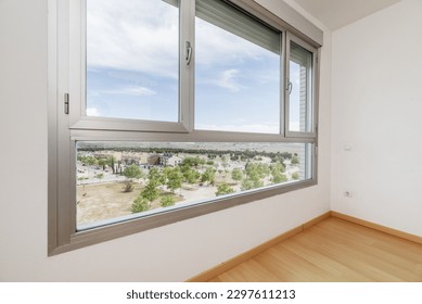 An empty room with a large window with unobstructed views of a park with young trees and other houses