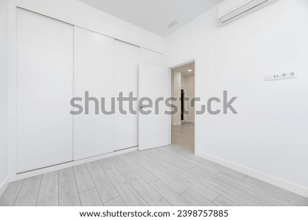 An empty room in a loft-type home with a built-in wardrobe that covers the entire wall with white wooden sliding doors