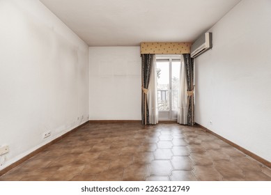 Empty room with old brown stoneware floor, wall mounted air conditioner and balcony with curtains and sheers - Powered by Shutterstock