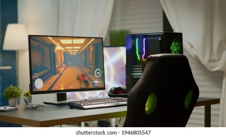 Empty room with RGB powerful personal computer for online videogames and gaming chair, first-person shooter game on screen. Cozy room with modern design is lit with warm and neon light.