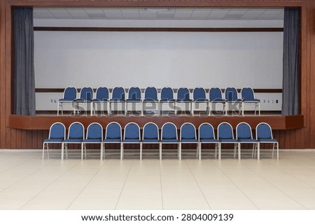 In an empty room, there are two arranged rows of chairs. One row is located on a pulpit, the other below on the floor. The chairs are blue and beige.