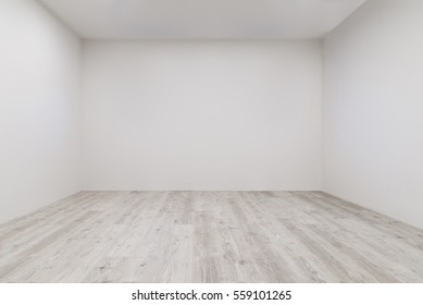 Empty room with whitewashed floating laminate flooring and newly painted white wall in background