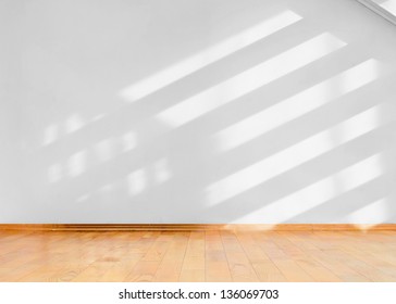 Empty Room With Wooden Floor And Diagonal Shadows On White Wall